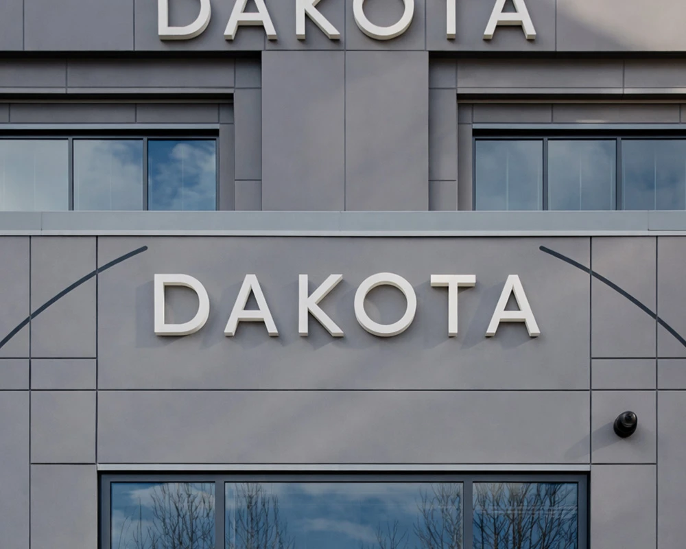 Close-up of a modern building façade with architectural cladding panels and prominent Dakota signage above glazed windows
