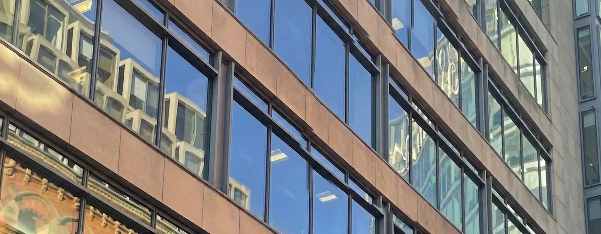 Angled view of a modern commercial building façade with metal cladding panels and reflective glazed windows in an urban setting